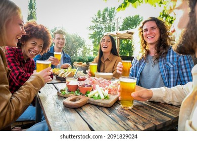 Group of multiethnic happy friends living healthy lifestyle and smiling and jocking while drinking beer at outdoor pub restaurant - Young people enjoying drinks during happy hour at bar