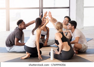 Group Of Multiethnic Happy People Giving High Five To Each Other After Training In Fitness Studio, Sitting In Yoga Mats And Smiling