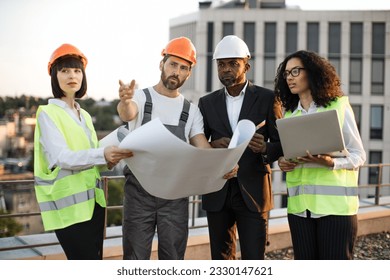 Group of multiethnic industrial employees planning building project and meeting on panoramic terrace. Four international colleagues using computer and technical plan for remodeling business center. - Powered by Shutterstock