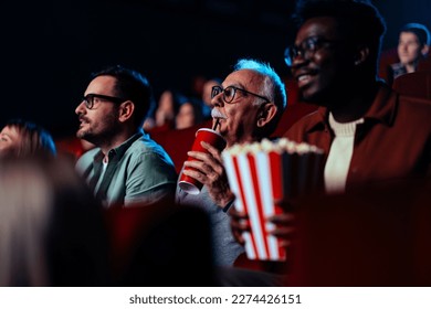 A group of multiethnic and multigenerational people are in the movie theater enjoying a movie on the big screen. - Shutterstock ID 2274426151