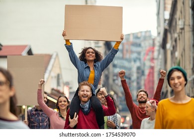 Group of multiethnic people on street holding blank cardboard placard celebrating victory during a protest. Group of content men and smiling women marching through a city. People protesting on road.