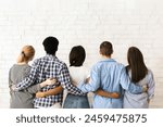 A group of multiethnic teenagers stands close together with their backs to the viewer, arms around each other in a display of friendship and unity, back view