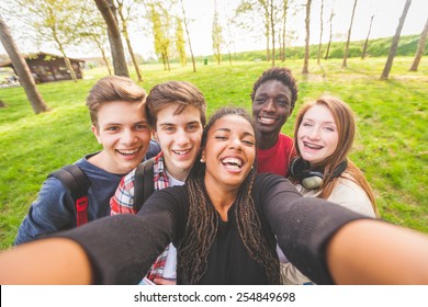 Group Of Multiethnic Teenagers Taking A Selfie At Park. Two Boys And One Girl Are Caucasian, One Boy And One Girl Are Black. Friendship, Immigration, Integration And Multicultural Concepts.