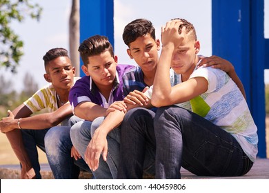 Group of multi-ethnic teens in park. Boys comforting sad friend