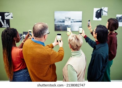 Grupo de visitantes multiétnicos escaneando el código QR para obtener más información sobre fotos en blanco y negro en la pared en la exposición en el museo Foto de stock