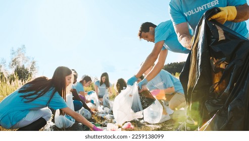 A group of multiethnic volunteers with the trash bags cleaning up the river. The eco activists in the gloves collecting garbage from the water. Nature, ecology survival, volunteering concept. - Powered by Shutterstock