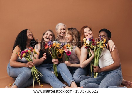 Group of multi-ethnic women sitting together in studio. Six smiling females with bouquets of flowers.