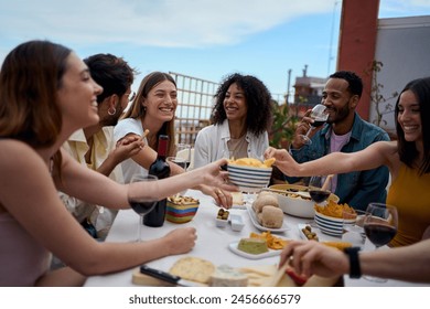 Group of multi-ethnic young friends enjoying meal gathered on rooftop. Happy millennial people having fun drinking red wine and eating celebrating a party event on summer day - Powered by Shutterstock