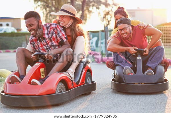 Group of\
multietnic friends having fun with go kart  - Young people with\
face mask on smiling and cheerful at mini car racing - Couples\
outside in double date - New\
lifestyle