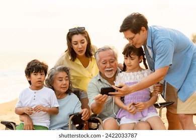 Group of Multi-Generation Asian family enjoy and fun outdoor lifestyle travel ocean together on summer holiday vacation. Happy family using mobile phone taking selfie together on the beach at sunset. - Powered by Shutterstock