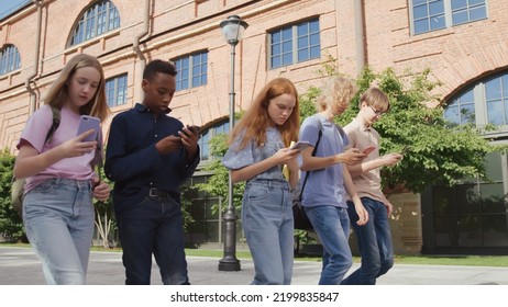 Group Of Multinational College Students Obsessed With Smartphones Walking Outdoors. Multiethnic Teens Use Cellphone Walking Together After School