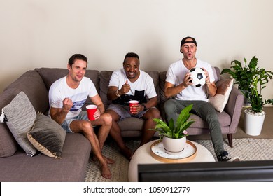 Group Of Multinational Guys Watching Football On TV With Excitement From Couch