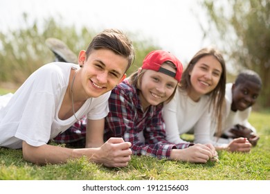 group of multinational modern teens lie in the park on the grass