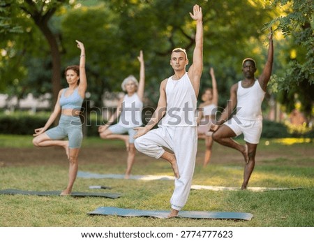 Group of multinational people practitioner performing Garudasana in sunny garden