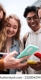 Group of multiracial classmate students looking at their smartphones sharing social media. Cheerful gathering outside university during daytime. Friends generation z having fun using mobile phone