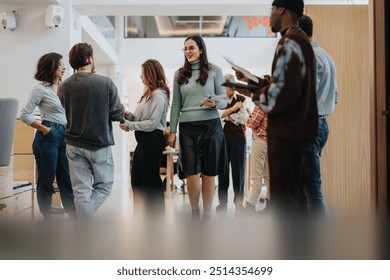 A group of multiracial colleagues engaging in a casual conversation in a brightly lit modern office space, exemplifying teamwork and networking. - Powered by Shutterstock