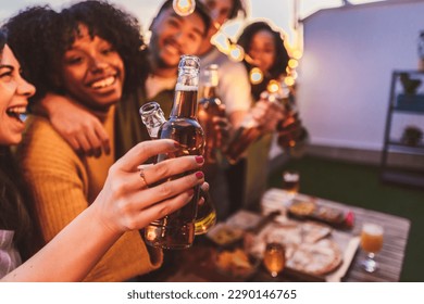 Group of multiracial friends drink beer on terrace and toast during summer evening - focus on beer bottle - - Powered by Shutterstock