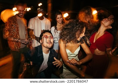 A group of multiracial friends is having a great time at the rooftop nightclub. They are dancing and clubbing at the night open-air party.