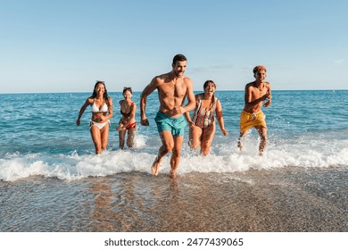 Group of multiracial friends running on the sand of the beach. Happy teenagers having fun coming out of the water fast, making a race to the seashore. Young people playing at the sea with swimm suit - Powered by Shutterstock