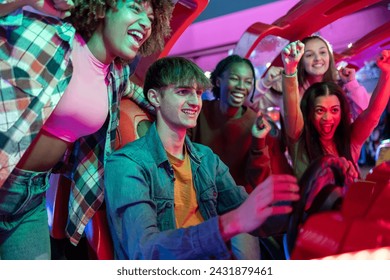 group of multiracial gamer friends playing racing arcade machines while celebrating excitedly - Powered by Shutterstock