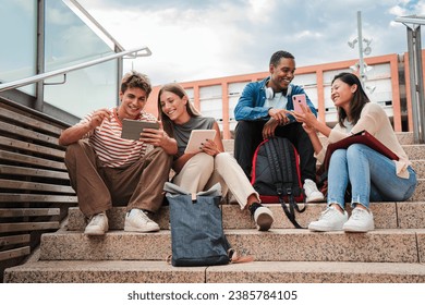 Group of multiracial high school students talking on a staircase at university campus, using a tablet app and smartphone to do homework project after class. Friendly teenage people studying together - Powered by Shutterstock