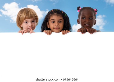 Group of multiracial kids portrait in studio with white board on blue sky background