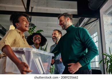 Group Of Multiracial People In The Office Talking With Their Colleague Who Return To Work And Carrying Plastic Box With Office Supplies