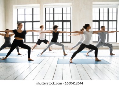 Group of multiracial people practicing yoga asanas, doing Warrior Two Virabhadrasana 2, work out indoors full length, posture increases stamina and flexibility, improves physical and mental endurance - Powered by Shutterstock