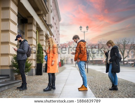 Group of multiracial people standing in a queue - Young people using mobile phones whilst waiting preventing corona - new normal keeping distance during lockdown and pandemic - Protective face mask