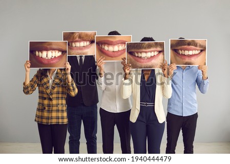Group of multiracial people standing in studio and hiding faces behind big funny mismatched closeup photos of happy positive attractive smiles. Humour, joke, clean teeth, successful dental care result
