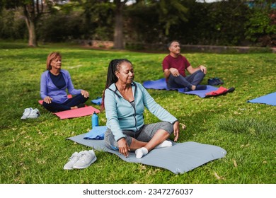 Group of multiracial senior people doing yoga meditation at city park - Fit elderly friends outdoor
