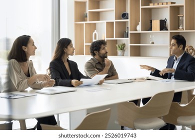 Group of multiracial students trainees of different age gender attend lecture seminar listen to Indian male coach mentor at meeting room. Project manager speak to teammates present benchmarking report