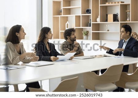 Group of multiracial students trainees of different age gender attend lecture seminar listen to Indian male coach mentor at meeting room. Project manager speak to teammates present benchmarking report