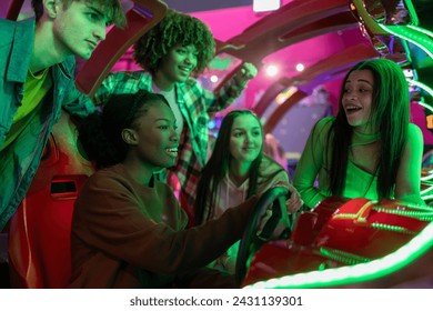 group of multiracial teenage friends in arcade playing car games with steering wheel