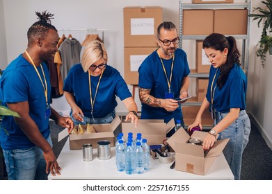 Group of multiracial volunteers wearing blue volunteer t shirt at donations stand separating donation stuff and putting them in a cardboard boxes. Concept of a charitable foundation. Diversity. - Shutterstock ID 2257167155