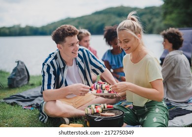 Group Of Multiracial Young Friends Camping In Campsite Near Lake And And Having Barbecue, Putting Skewers O Grill.