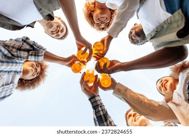 group of multiracial young people clink beer bottles outdoors, interracial students celebrating toast and relaxing together, six bottles of alcohol holding hands, bottom view - Powered by Shutterstock