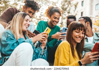 Group of multiracial young people using smart mobile phone device outdoors - Happy university students watching cellphones sitting in college campus - Teenagers addicted to social media technology 