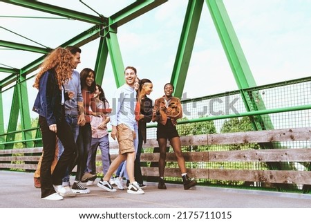 a group of multiracial young people walking together crossing a bridge on a weekend day - lifestyle concept of friendship, brotherhood - focus on the man in the center