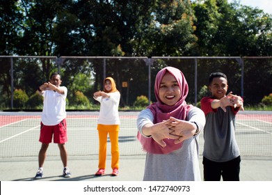 Group Of Muslim Asian People Get Warm Up And Streching Their Body At Outdoor Tennis Hard Court On Sunny Day