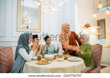 group of Muslim friends clapping happily when one of their friends is given a surprise gift at the dinner table
