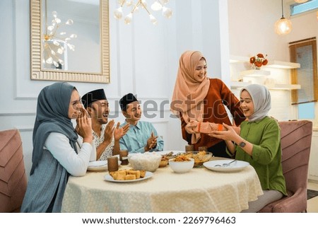 group of Muslims celebrating and giving gifts to veiled woman while gathering at a dinner table