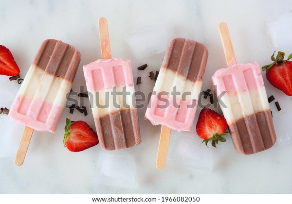 Group of neapolitan yogurt ice pops.\
Above view in a row on a white marble\
background.
