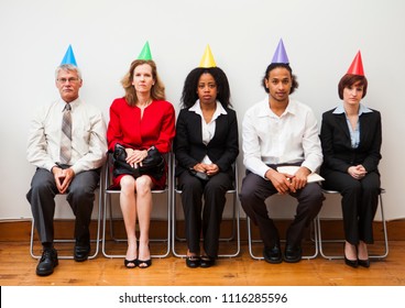 A Group Of Office Workers Looking Bored Or Disinterested While Wearing Party Hats. Humorous Business Concept.