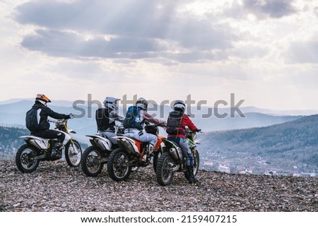 group of off-road dirt motorcyclists standing on edge of cliff  with a beautiful mountain valley  view 