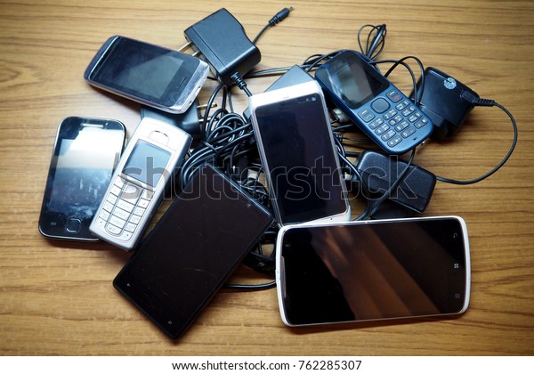 Group of old mobile phones and chargers on a\
wooden table. Photo taken before they\'re donated to an organization\
for recycle.