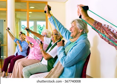 Group Of Older Women Seated In Chairs Using Stretching Bands For Physical Fitness Class