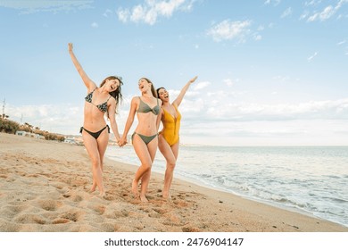 Group of only women smiling and walking on the sand of the beach, enjoying their summer vacations. Three pretty young girls sightseeing at sea shore wearing a bikini swimsuit on a sunny day. High - Powered by Shutterstock