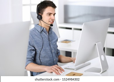 Group of operators at work. Call center. Focus on young man receptionist in headset at customer service. Business concept and casual clothing style