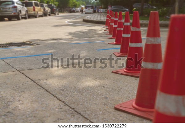Group of orange traffic pylon blocking vehicles on\
street. Traffic cones use for the road closed or restricted area\
with sun light background. Selective focus and safety or security\
concept. 